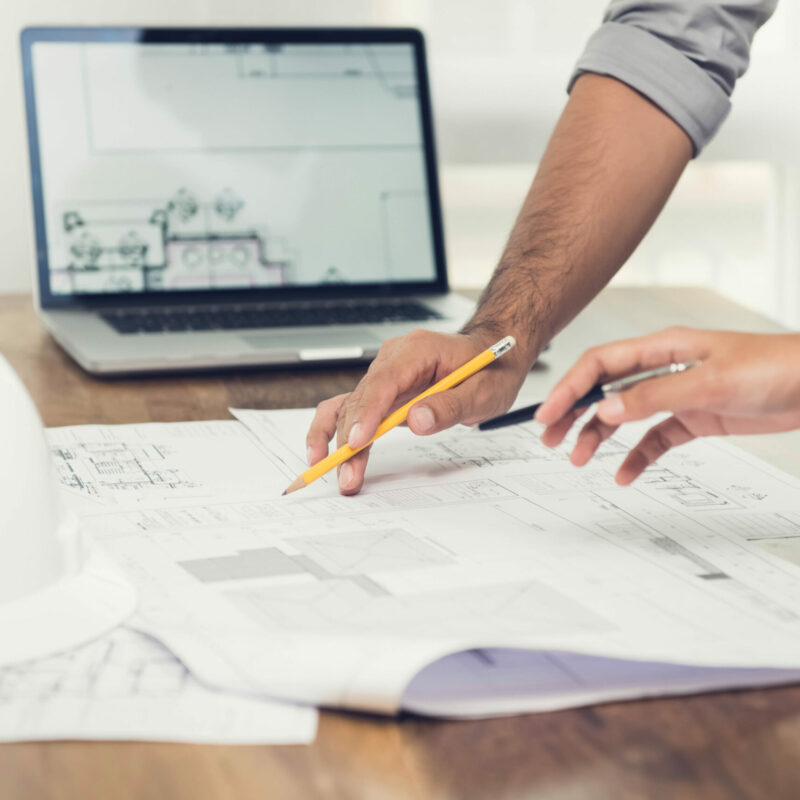 Architect or engineer team discussing a project design using blueprints and a laptop computer at the office before visiting work site.